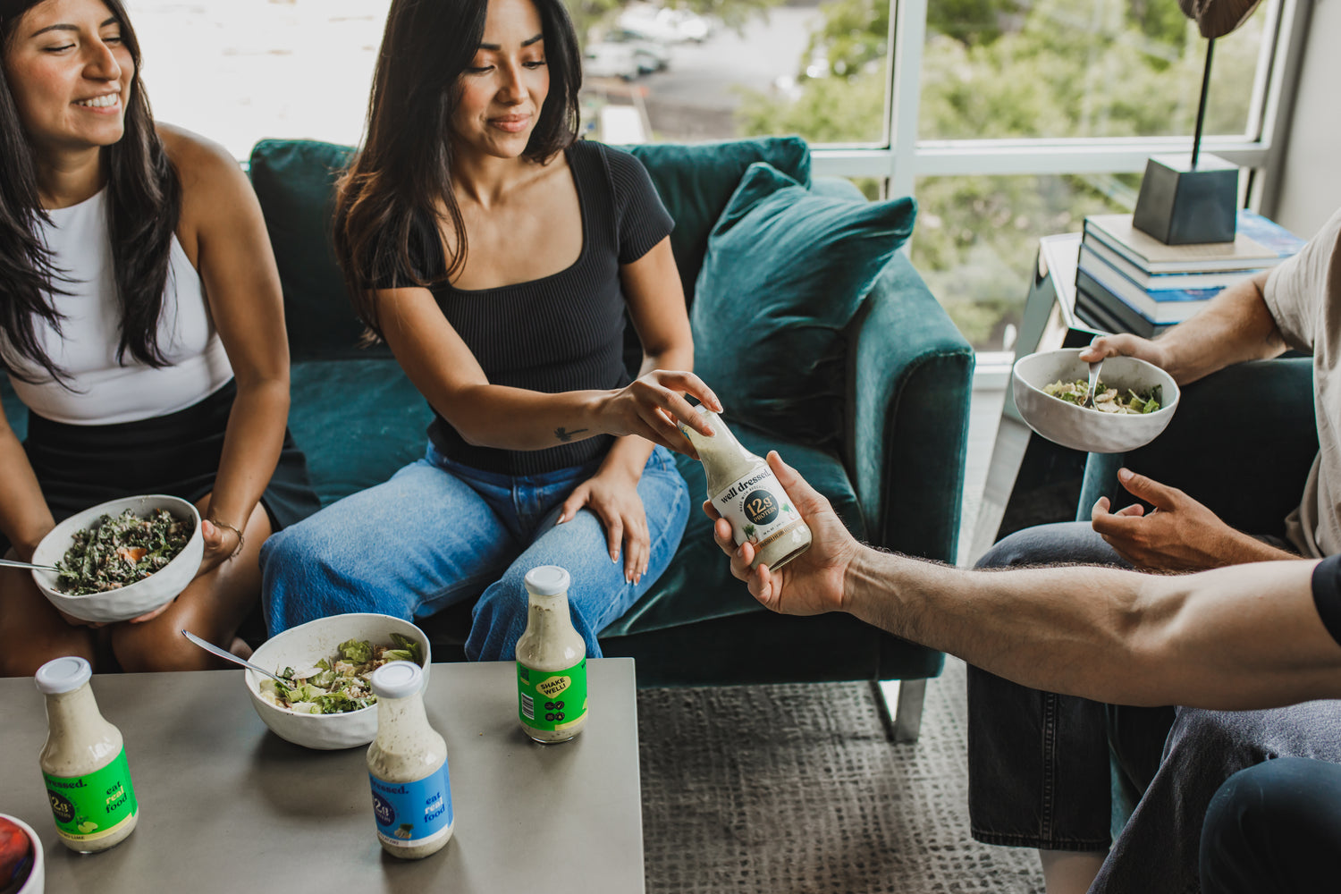 group of people smiling with bowls of salad dressing on the table and bottles of salad dressing. 